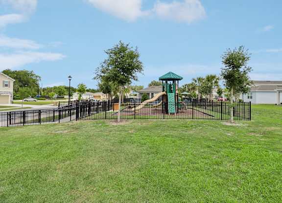 A playground with a green slide and a black fence.