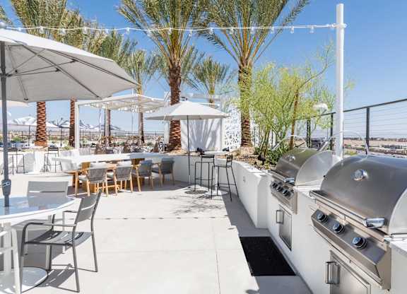 A patio with a grill and chairs under umbrellas.