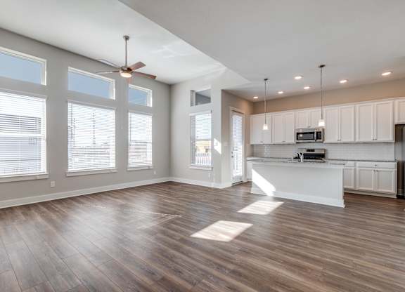 Houston, TX, Rental Homes - East Heights - Unfurnished Living Room with Vinyl Plank Flooring, Ceiling Fan, Large Windows, and View of Kitchen.