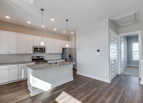 Rental Homes in Houston, TX - East Heights - Kitchen with Vinyl Plank Flooring, White Cabinetry, Stainless Steel Appliances, Granite Countertops, Kitchen Island with Pendant Lights, and Tile Backsplash.