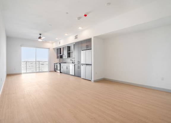 A large empty room with wooden floors and a kitchen area in the background.