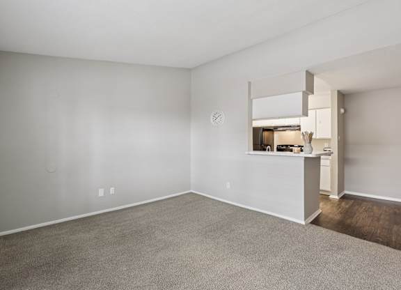 A large, empty room with a carpeted floor and a small kitchen area in the background.