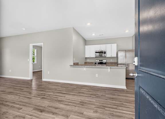 A room with a kitchen area and a doorway leading to another room.