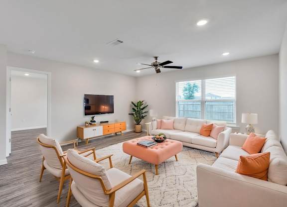 A living room with a white couch, a pink ottoman, and a wooden chair.