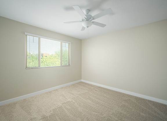 A room with a ceiling fan and a window with blinds.