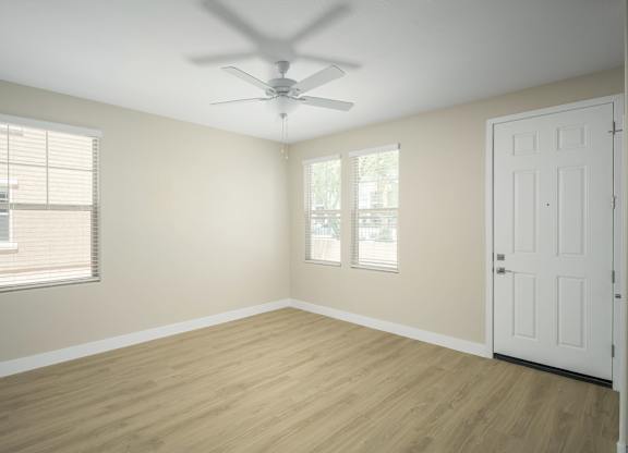 A room with a white door, a ceiling fan, and a window with blinds.