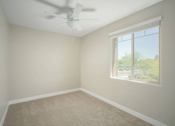 A room with a ceiling fan and a window showing a view of trees.