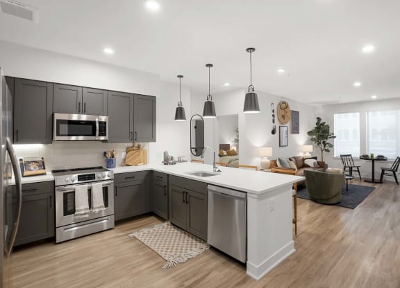 Apartments for Rent in Castle Rock, CO - Alana - Kitchen with Luxury Plank Flooring, Hanging Light Fixtures, Kitchen Island, Quartz Counters, Brown Cabinets, White Tile Backsplash, and Stainless-Steel Appliances