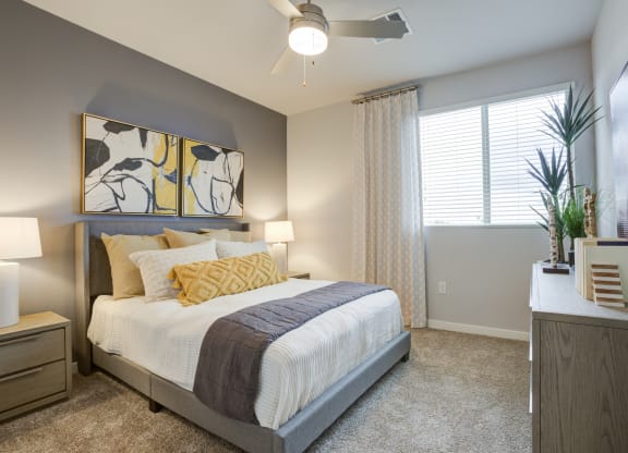 South Scottsdale Apartments - Lucent Scottsdale - Spacious Bedroom With Carpeted Flooring, Bed, Side Tables With Lamps, Dresser, Ceiling Fan, And A Window With Blinds