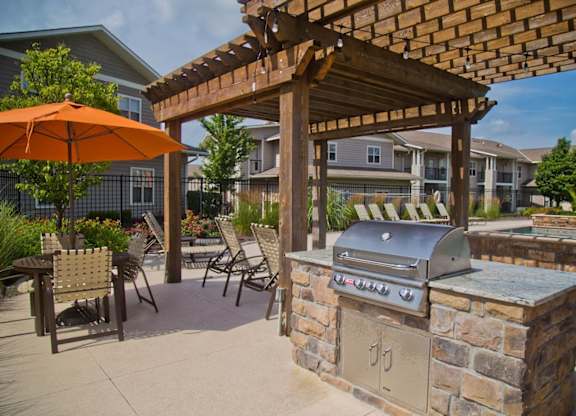 A patio with a grill and chairs under a wooden pergola.