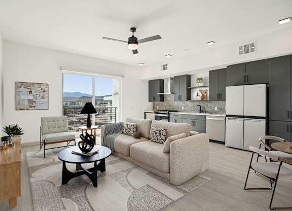 A modern living room with a large window and a kitchen in the background.