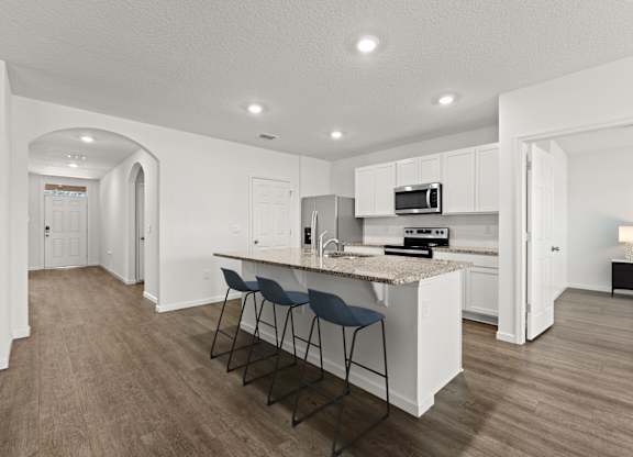 A kitchen with white cabinets and a countertop with a bar stool.