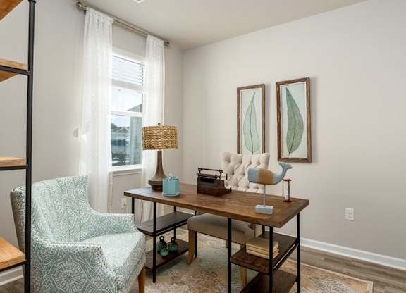 a home office with two paintings on the wall and a wooden desk with a chair and a