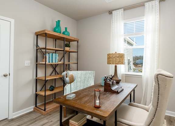 a home office with a large window and a wooden bookshelf
