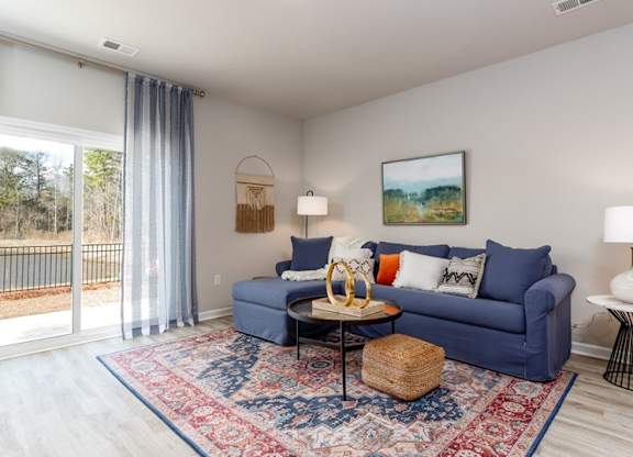 Houses for Rent in Myrtle Beach - The Palmer at Carolina Forest - Living Room with a Blue Sectional Couch, a Large Rug, Vinyl Plank Flooring, and a Sliding Glassdoor