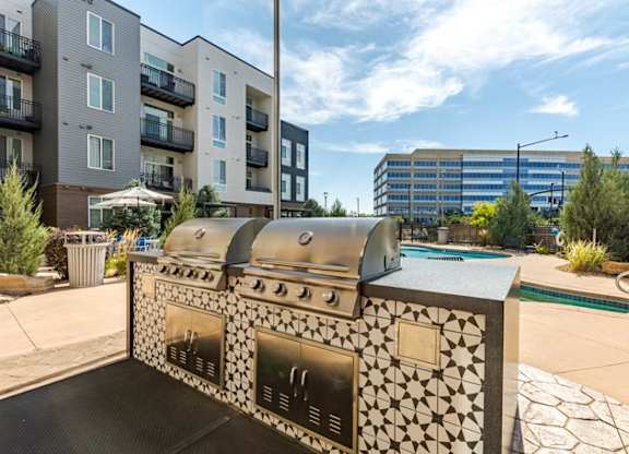 an outdoor grill with a pool and an apartment building in the background