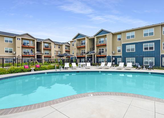 Vancouver, WA, Luxury Apartments with In-Unit Washer and Dryer - Autumn Grove Apartments - Swimming Pool Area Surrounded by Lounge Chairs and Modern Three-Story Buildings.