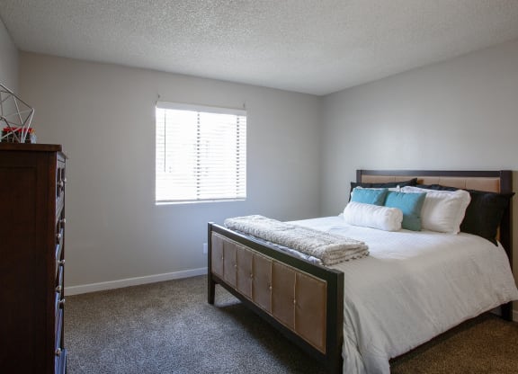 Tucson, AZ, Apartments Near University of Arizona - Peaks at Redington - Bedroom with Carpet Flooring, Large Bed, Dresser, Home Decor, and Window with Blinds.