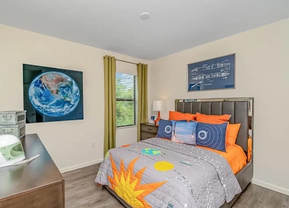 A bedroom with a bed, a dresser, and a painting of the Earth on the wall.
