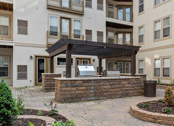 A patio with a table and chairs is surrounded by a stone wall and a garbage can.