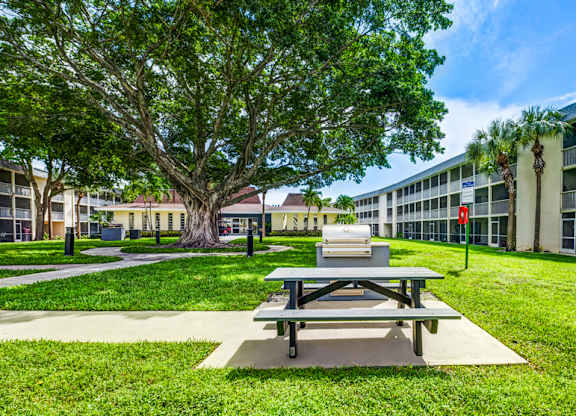 Green courtyard with picnic tables at Coronado Springs Apartments in Palm Springs, FL. Pet-friendly outdoor space for residents to relax.