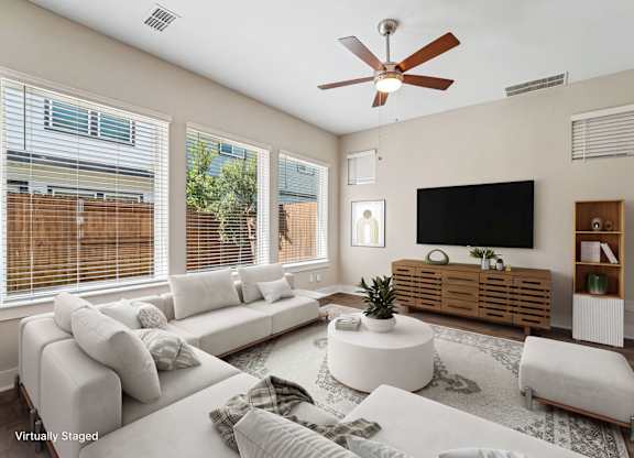 A living room with a white couch, a flat screen TV, and a ceiling fan.