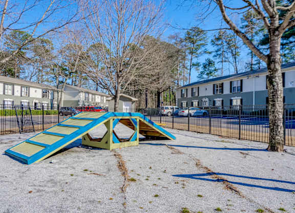 A playground with a blue and yellow slide in the foreground and apartment buildings in the background.