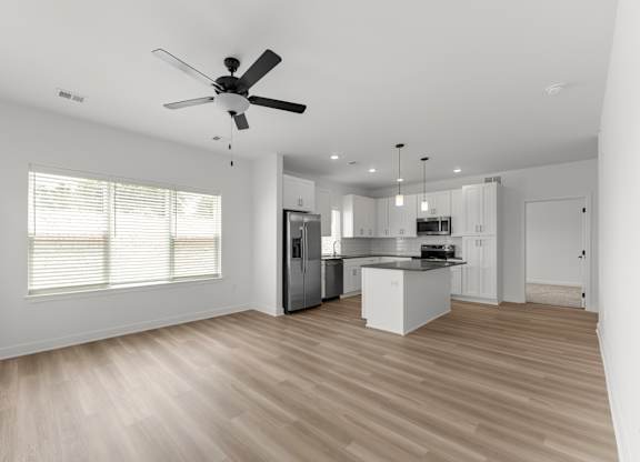 A spacious kitchen with a ceiling fan and wooden flooring.