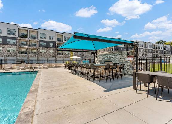 A swimming pool with a blue canopy and chairs around it.