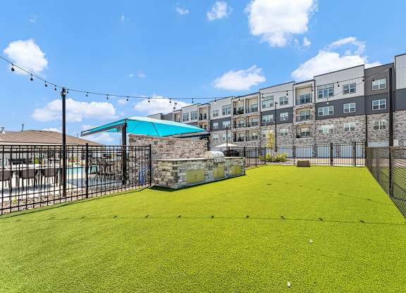A green artificial turf soccer field with a fence and a building in the background.