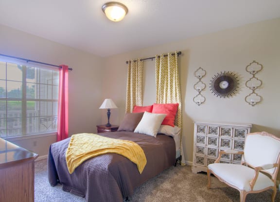 Enclave at Wolfchase Apartments in Cordova Tennessee photo of a bedroom with a bed and a chair in front of a window