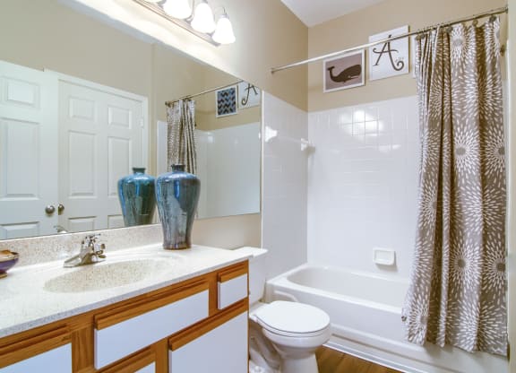 Enclave at Wolfchase Apartments in Cordova Tennessee photo of a bathroom with a white toilet next to a bathtub with a shower curtain