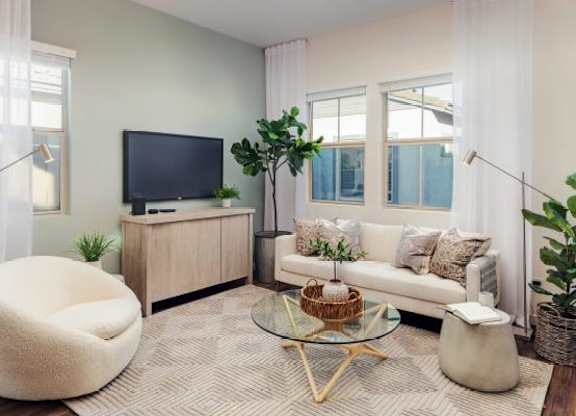 A living room with a white couch, a white chair, a glass coffee table, and a television on a cabinet.