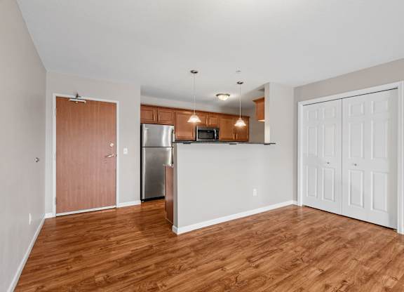 an empty living room with wood flooring and a kitchen with stainless steel appliances