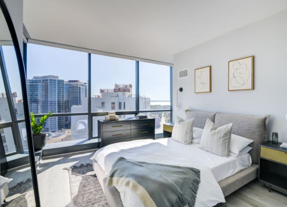 Bright and airy city-view bedroom with a comfortable bed adorned with white and grey pillows, flanked by minimalist nightstands and abstract wall art.