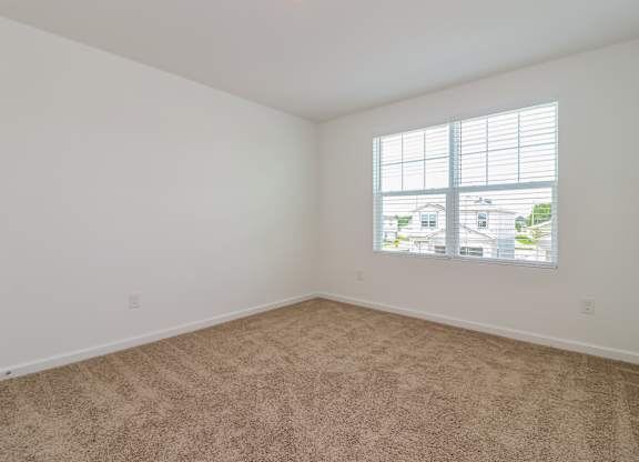 A room with a carpeted floor and a window showing a view of houses.
