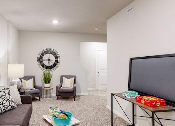 A living room with a grey couch, a yellow pillow, a white lamp, a round mirror, a small table with a box of tissues and a bowl of fruit.