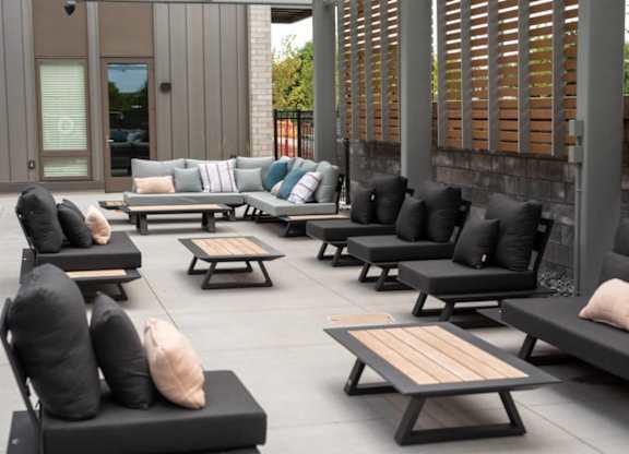 A patio with black cushioned furniture and wooden tables.