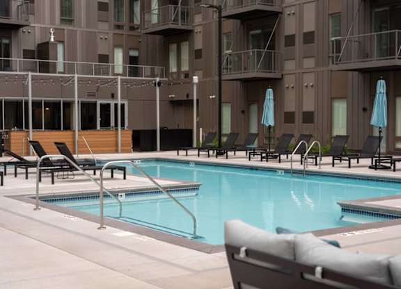 A pool surrounded by chairs and umbrellas in front of a building.