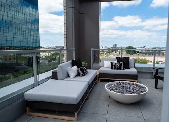 A balcony with two grey cushioned seats and a bowl of stones in the middle.
