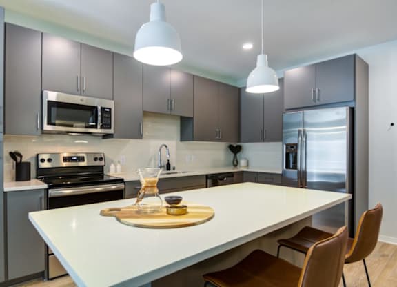 A modern kitchen with a white island and brown chairs.