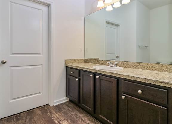A bathroom with a white door, brown cabinets, and a marble countertop.