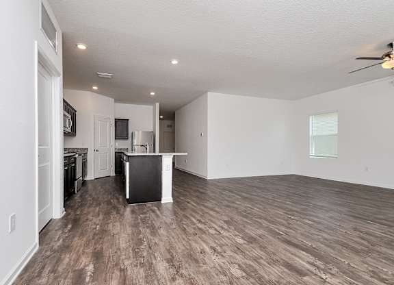 A spacious living room with a kitchen in the background.