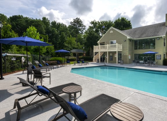 a swimming pool with chairs and umbrellas next to a house