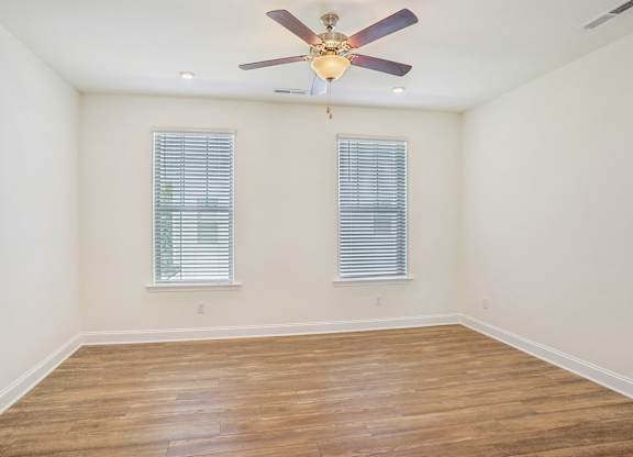an empty room with a ceiling fan and two windows