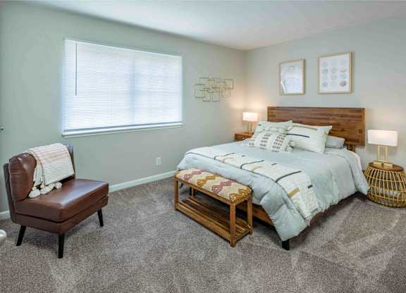 A bedroom with a bed, chair, and nightstand.