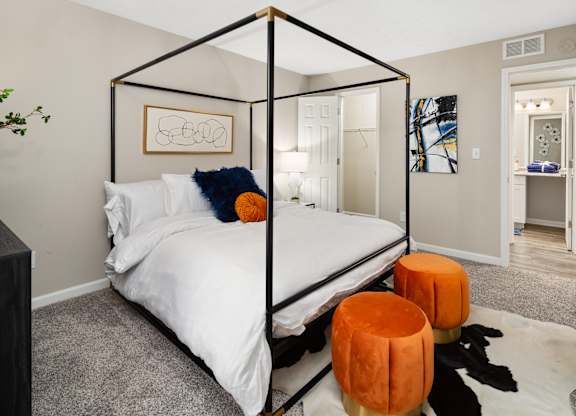 A bedroom with a four poster bed and orange stools.