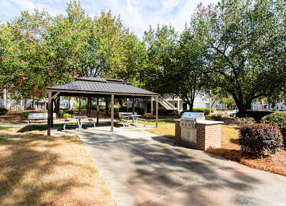 A gazebo is surrounded by trees and a brick wall in a park.