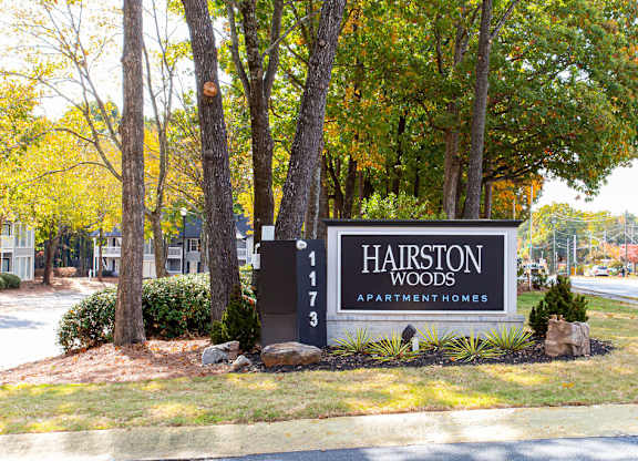 A sign for Hairston Woods Apartment Homes is in front of a row of trees.