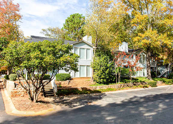 A house with a white door and windows is surrounded by trees with autumn leaves.